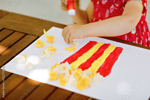 Little creative toddler girl painting with finger colors popcorn box and making paper corns with glue. Active child having fun with drawing doing handicraft. Education for kids. Creaitve activity. photo