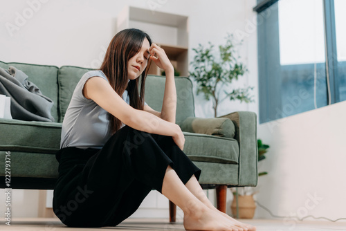 Depressed Asian woman sitting next to the sofa sad, feeling tired, lonely and unhappy.