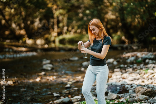 Beautiful young red haired woman relaxes after running. He walks by the river and enjoys nature.  Healthy lifestyle and sport in nature concept. photo