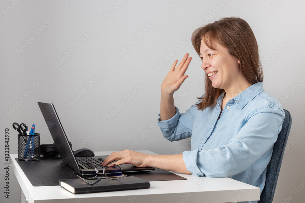 Happy smiling woman or teacher female sitting at table at home office with laptop looking at the camera and greeting people for video call webinar, conference or online course Happy smiling woman or teacher female sitting at table at home office with laptop looking at the camera and greeting people for video call webinar, conference or online course