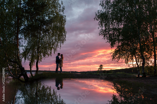 A couple in love, a guy and a girl are standing facing each other in full height, on the seashore at sunset, the couple’s reflection in the water, pink sunset, nature, love story, holiday, Valentine’s