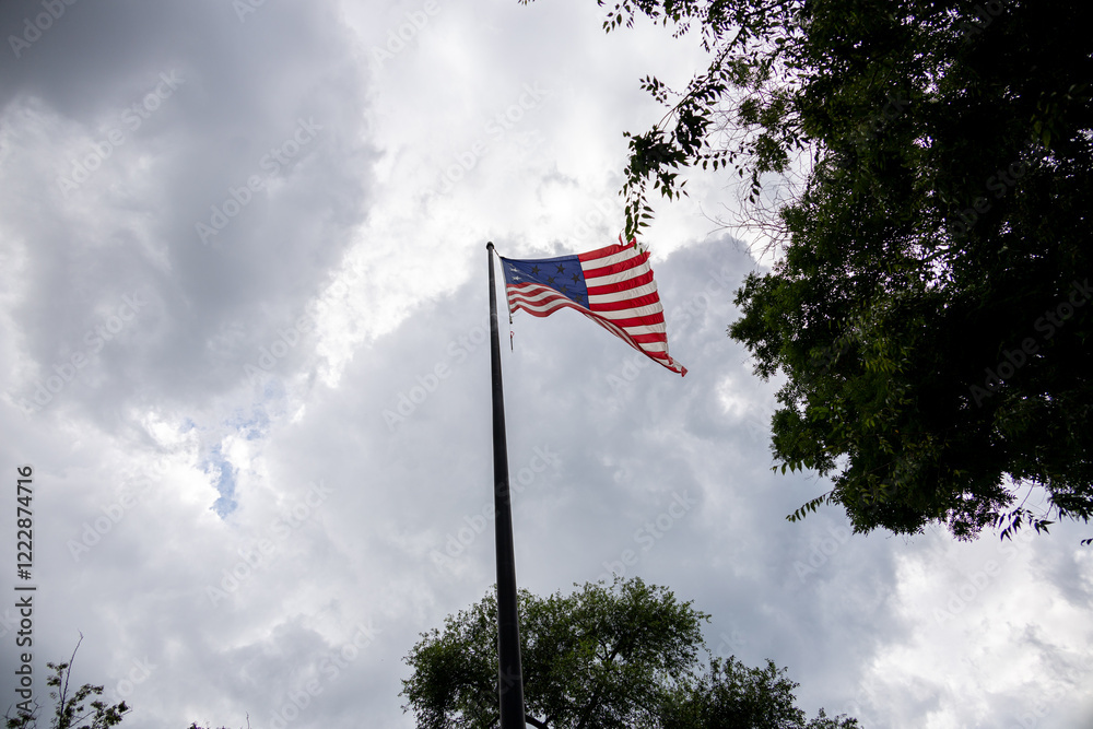 The United States flag waving against a cloudy sky, representing patriotism and national pride amidst dramatic weather.