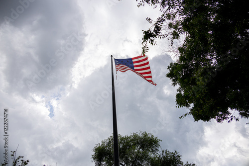 Obraz na płótnie The United States flag waving against a cloudy sky, representing patriotism and national pride amidst dramatic weather. w salonie