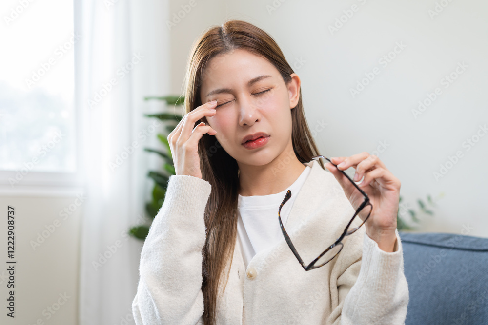 Eye care problem concept, fatigue asian young woman tired eyes irritated rubbing, massage eye dry relief vision pain sitting on couch, sofa at home, eye strain, hand holding glasses, suffer bad blurry Eye care problem concept, fatigue asian young woman tired eyes irritated rubbing, massage eye dry relief vision pain sitting on couch, sofa at home, eye strain, hand holding glasses, suffer bad blurry