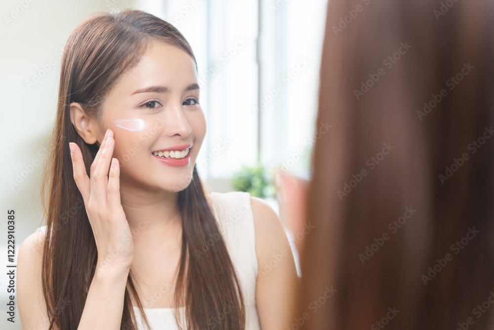 Facial beauty skin health care, smile of cute asian young woman looking at mirror, hand applying moisturizer lotion on her face, female putting cream treatment before makeup cosmetic routine at home. Facial beauty skin health care, smile of cute asian young woman looking at mirror, hand applying moisturizer lotion on her face, female putting cream treatment before makeup cosmetic routine at home.