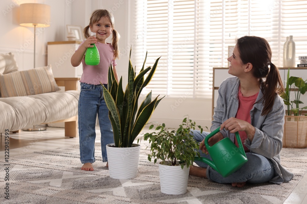 Fototapeta premium Cute little girl helping her mother watering houseplants at home
