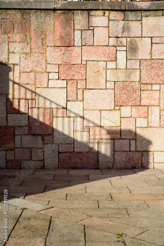 Sombra de barandilla sobre pared de placas cuadradas de piedra rosada