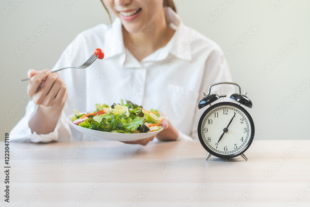 Intermittent fasting concept, close up clock, asain young woman, girl diet eating ketogenic low carb, fresh green vegetable salad on plate. Eat food healthy first meal in morning on table at home. Intermittent fasting concept, close up clock, asain young woman, girl diet eating ketogenic low carb, fresh green vegetable salad on plate. Eat food healthy first meal in morning on table at home.