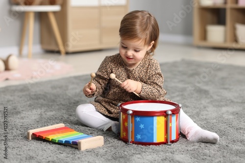 Cute little girl playing with toy musical instruments on floor at home