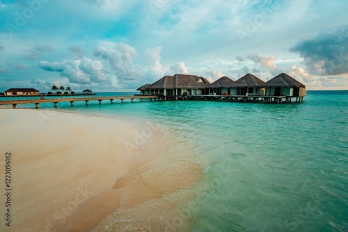 Fototapeta Naklejka Na Ścianę i Meble -  Overwater bungalows in a tropical paradise with turquoise waters and a sandy beach under a blue sky.