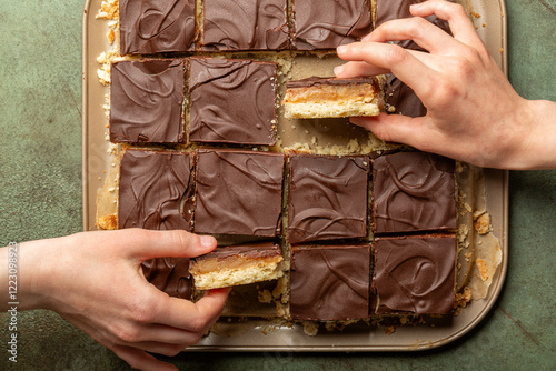 Cuadro en lienzo Girls hand taking a piece of Caramel shortbread, also known as caramel squares, slice, or millionaire's shortbread