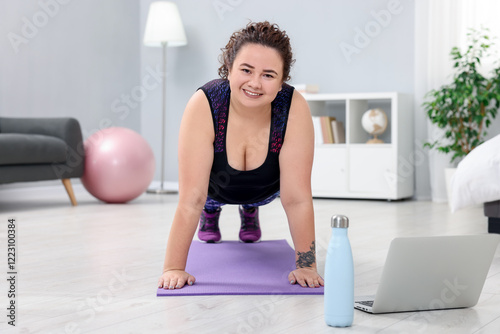 Plus size woman having fitness training with online coach via laptop at home