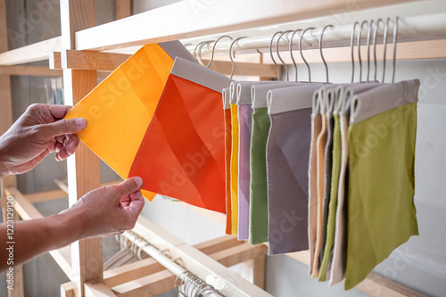 Stylist hand comparing fabric pieces from fabric swatch material. Upholstery sample collection hanging on showcase rack. Textile industry for home interior design and furniture finishing decor