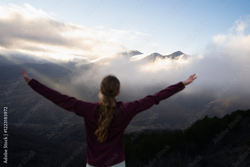 Background focus. Woman hiker stands with raised hands on top of the mountain against background of sunset. Discovery, destination, travel, hiking, tourism. Sport, healthy lifestyle. Background focus. Woman hiker stands with raised hands on top of the mountain against background of sunset. Discovery, destination, travel, hiking, tourism. Sport, healthy lifestyle.