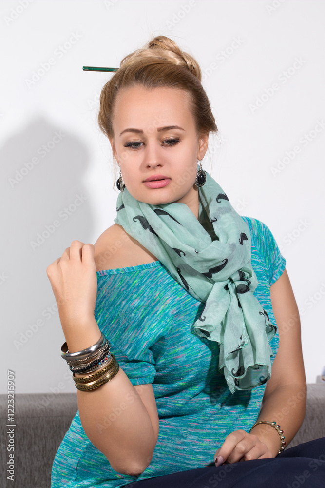 Pensive woman with scarf and bracelets sitting on sofa