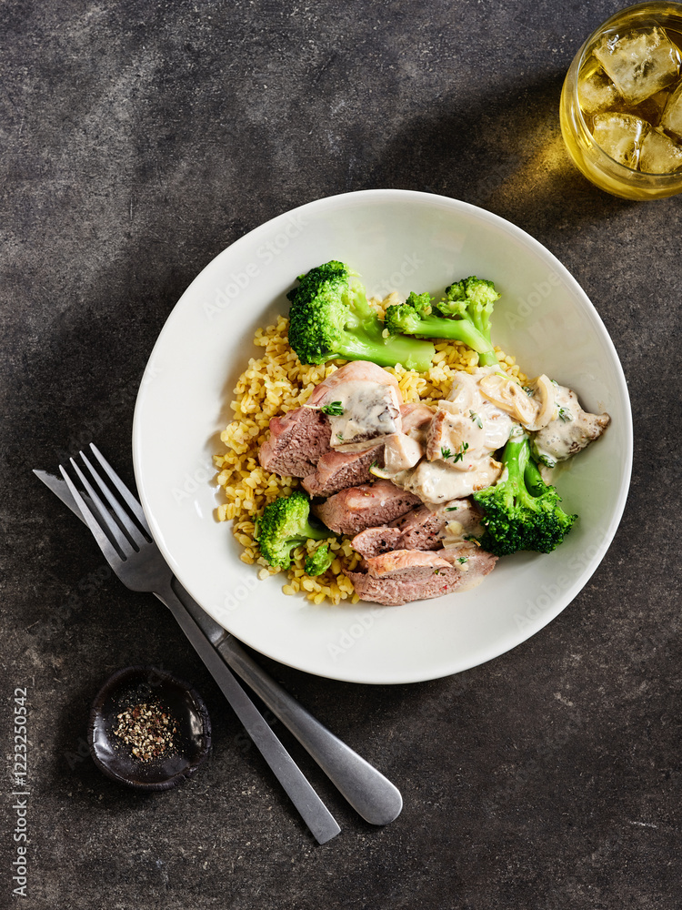 A beautifully arranged plate features tender slices of grilled meat paired with vibrant broccoli and creamy sauce over a bed of grains. Cold drink accompanies the dish A beautifully arranged plate features tender slices of grilled meat paired with vibrant broccoli and creamy sauce over a bed of grains. Cold drink accompanies the dish