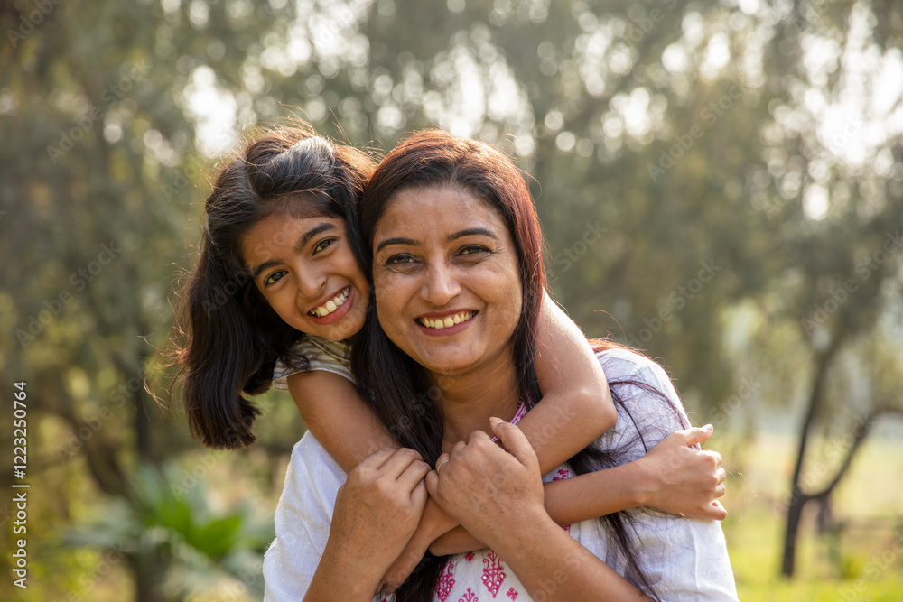 Fototapeta premium Indian mother and daughter embracing each other. Indian mother holding her lovely daughter at park. cheerful daughter enjoying a ride on the back of her mother. Mom and daughter love, parent hugging