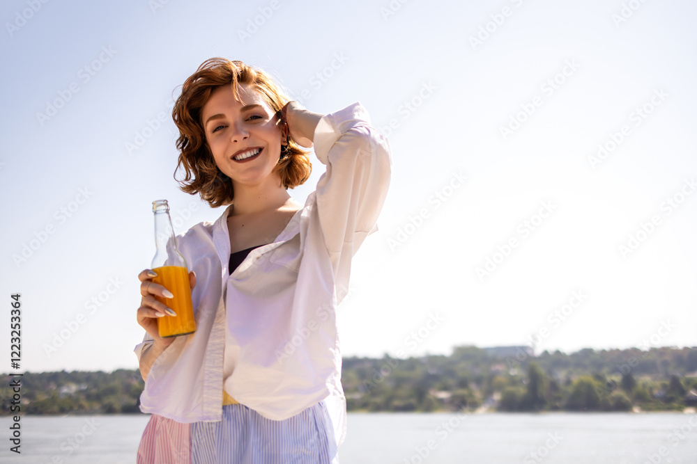 Portrait of young ginger woman posing at the camera at the beach while she drinks cocktail. Portrait of young ginger woman posing at the camera at the beach while she drinks cocktail.