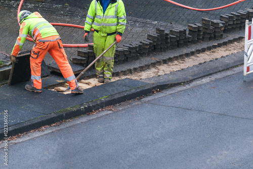 Konzept Glasfaserausbau, Internet, Kommunikation und: Arbeiter bei Baumaßnahmen für die Verlegung von Glasfaserleitungen für den Hausanschluss in einer Straße photo