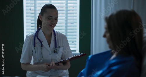 Doctor beside elderly patient in hospital room, presenting paperwork for her to sign.
