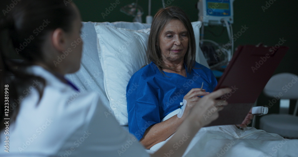 Obraz premium Young doctor offers paperwork for elderly patient to sign while seated beside her.