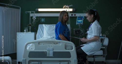 Young doctor conducts a throat examination on the elderly patient in the hospital ward, palpating her neck for signs of discomfort.