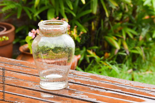 Clear glass vase in the rain on a wooden table with plants background