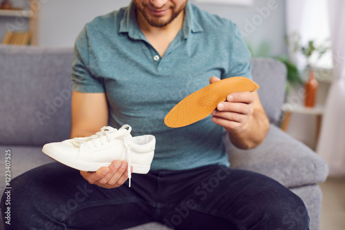 Man putting new orthopedic insole into sport shoe, white sneaker for walking, running. Foot care, flat feet, orthopedic diseases prevention, wearing comfortable medical orthotic shoes to relieve pain photo