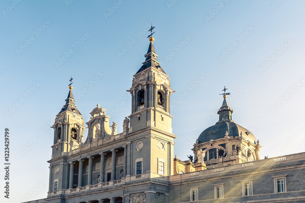 Detail of the Almudena Cathedral in Madrid, highlighting the twin bell towers and central dome under clear skies, Spain. The neoclassical style of the facade is adorned with columns and statues Detail of the Almudena Cathedral in Madrid, highlighting the twin bell towers and central dome under clear skies, Spain. The neoclassical style of the facade is adorned with columns and statues