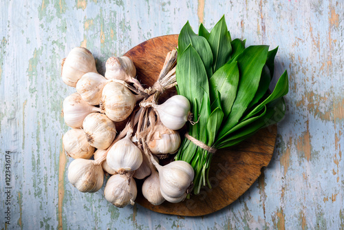 Garlic heads and fresh bear's wild garlic leaves on wooden cutting board close up. Food photography, top view