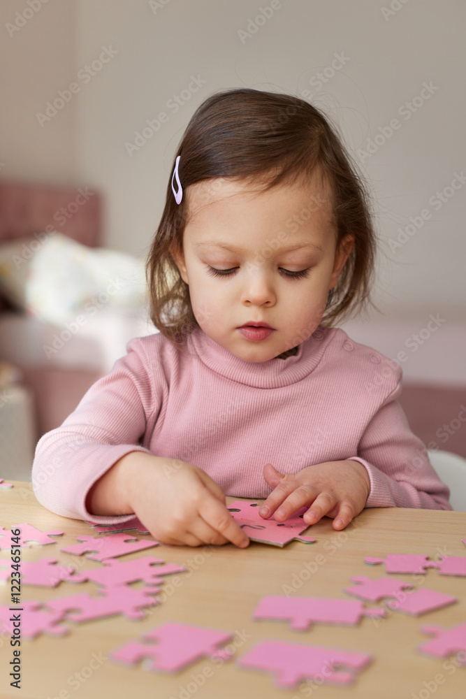 Cute little child girl connecting puzzle pieces on wooden desk in room, children development Cute little child girl connecting puzzle pieces on wooden desk in room, children development