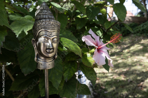 Buddha statue in green bush leaves with pink flower. Vesak day, Purnima, spring flowers festival, Songkran. Background, copy space, text place photo