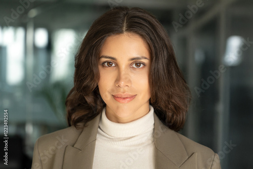 Closeup headshot face portrait of beautiful successful hispanic young business woman looking confident at camera. Smiling latin or eastern middle age female ceo leader businesswoman standing in office