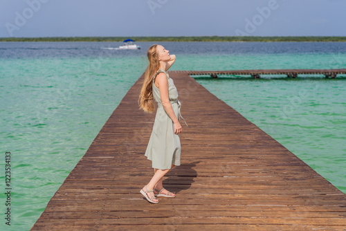 Female tourist in a turquoise dress standing on a wooden pier over the turquoise waters of Bacalar Lake, Mexico. Peaceful tropical travel destination concept photo