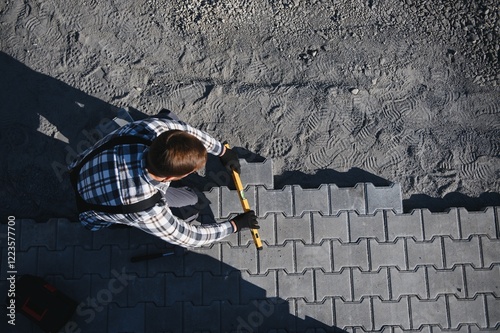 The master in gloves lays paving stones in layers. Garden brick pathway paving by professional paver worker. Laying gray concrete paving slabs in house courtyard on sand foundation base