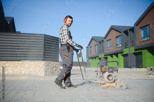 Landscaping worker using vibratory tamping machine plate compactor on a new patio driveway pavement to apply Polymeric sand to fill joint