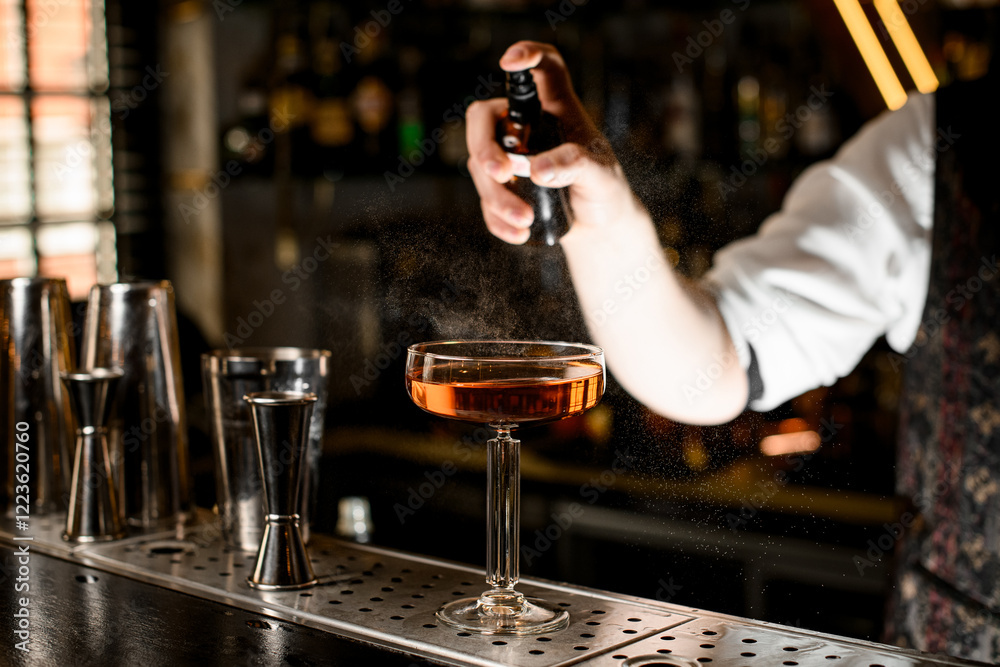 Focus on stemmed wine glass filled with brown cocktail being sprayed Focus on stemmed wine glass filled with brown cocktail being sprayed
