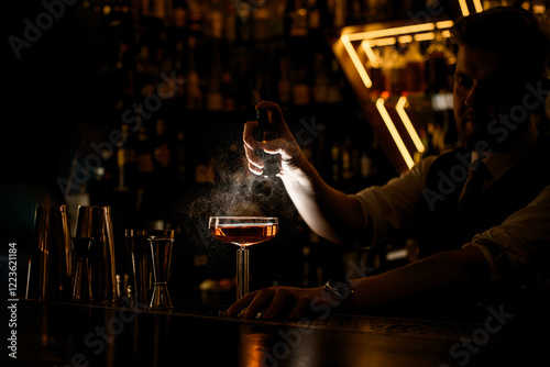 Bartender sprays glass with brown cocktail, on bar counter