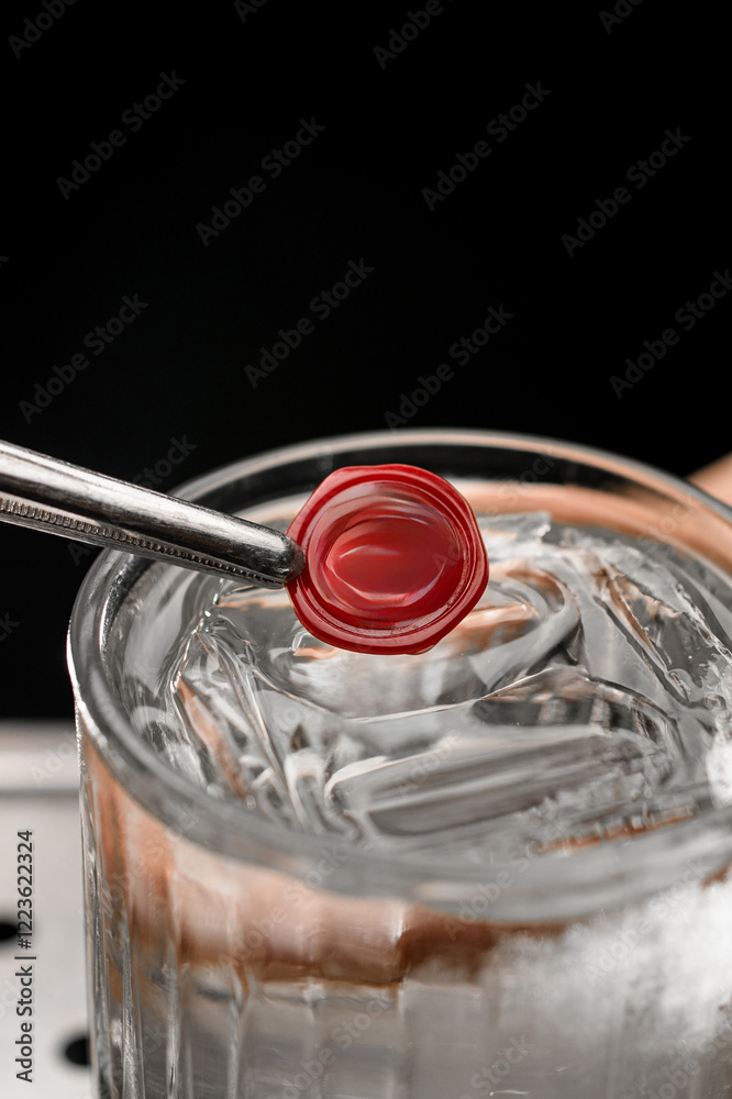 Φωτογραφία Red crushed seal is held with tweezers directly above a glass with an iced cockt