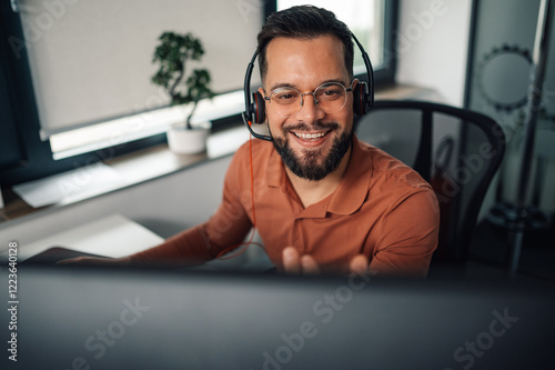 Smiling male call center agent working on computer in office