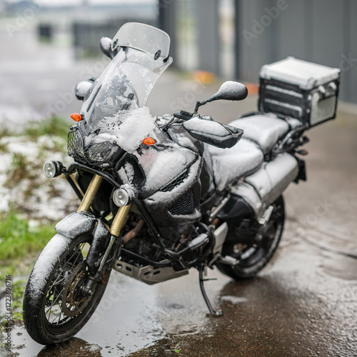 A large black touring motorcycle is covered in snow. The end of the motorcycle season, winter. The inscriptions 
