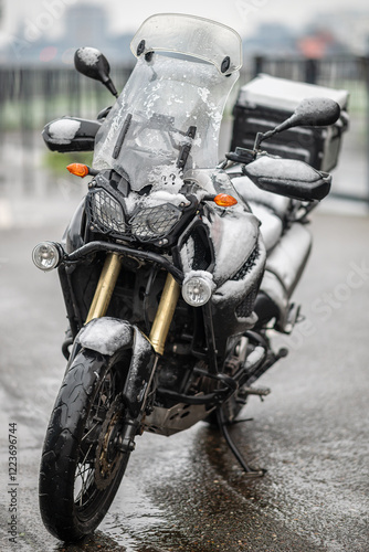 A large black touring motorcycle is covered in snow. The end of the motorcycle season, winter. The inscriptions 