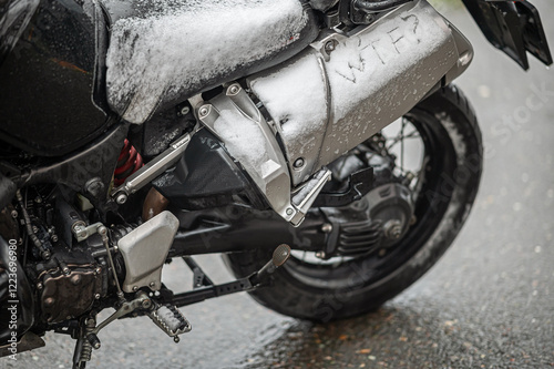 A large black touring motorcycle is covered in snow. The end of the motorcycle season, winter. The inscriptions 