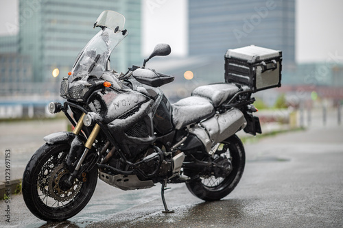 A large black touring motorcycle is covered in snow. The end of the motorcycle season, winter. The inscriptions 