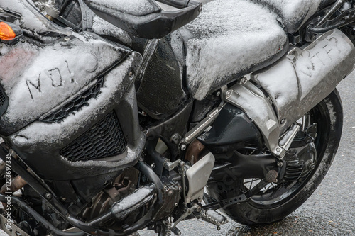 A large black touring motorcycle is covered in snow. The end of the motorcycle season, winter. The inscriptions 