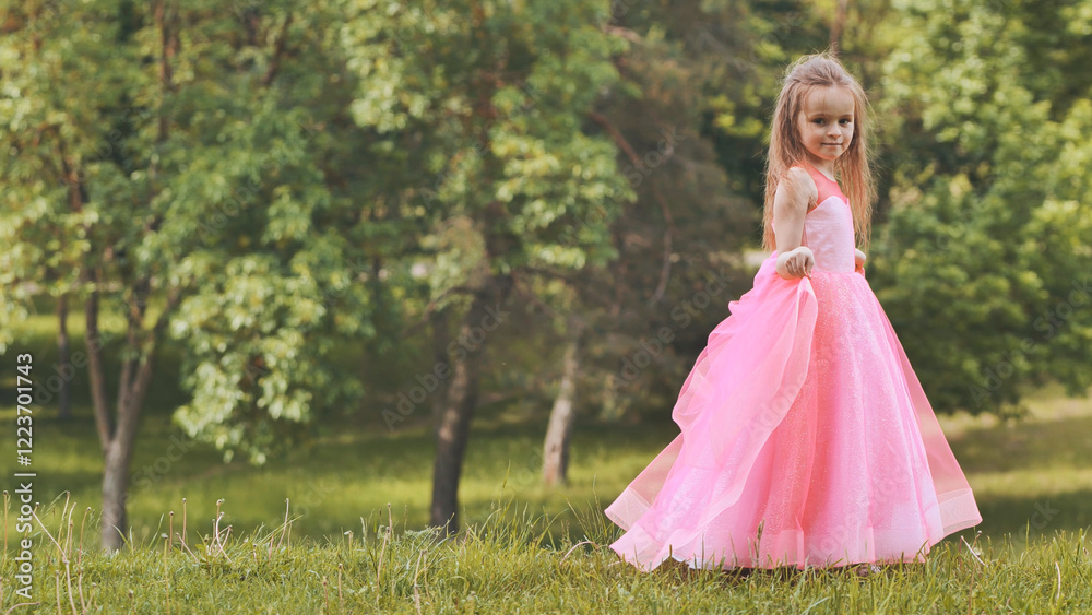 Young girl in pink princess dress posing near grassy meadow, sunlight illuminating delicate dress details Young girl in pink princess dress posing near grassy meadow, sunlight illuminating delicate dress details