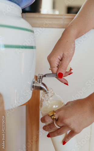 Close-up of hands pouring liquid from a dispenser into a glass bottle