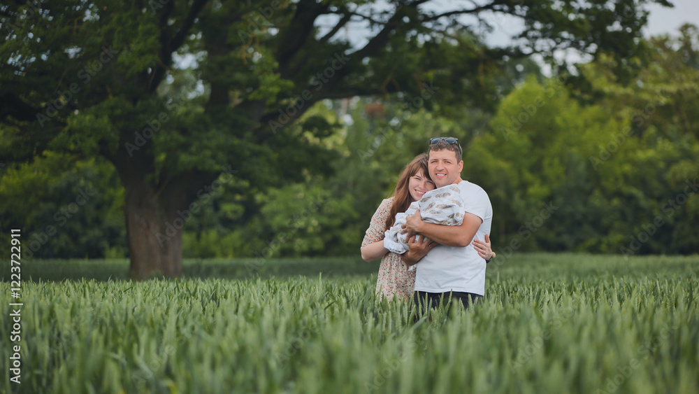 Parents holding their newborn baby in a green wheat field under a big tree, enjoying a peaceful family moment in nature Parents holding their newborn baby in a green wheat field under a big tree, enjoying a peaceful family moment in nature