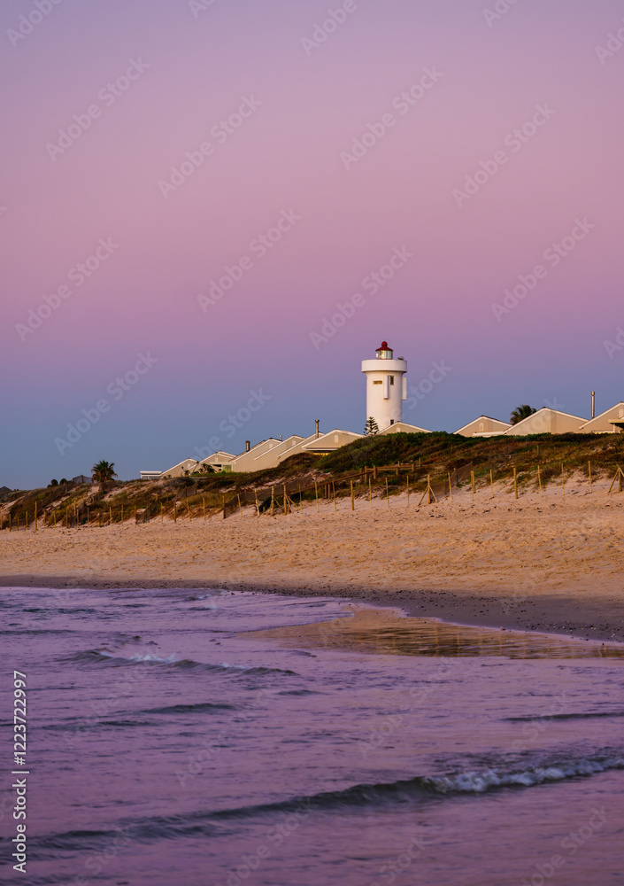 Vertical shot of Woodbridge Island Lighthouse during a stunning sunset twilight, with warm golden hues reflecting on the calm waters, Cape Town, South Africa