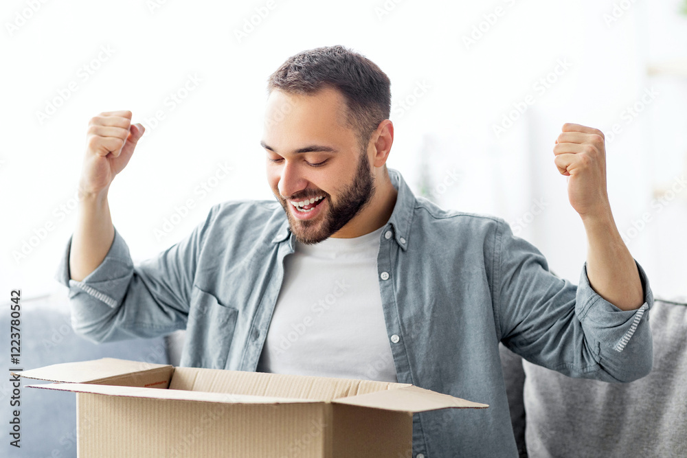 Satisfied male client opening cardboard box, excited over good delivery service, receiving online store order, making YES gesture at home. Young guy unpacking parcel in living room Satisfied male client opening cardboard box, excited over good delivery service, receiving online store order, making YES gesture at home. Young guy unpacking parcel in living room